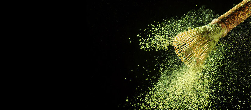 Bamboo whisk with flying matcha tea powder on black background with copy space.