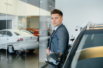 A young businessman looks at a new car in a car dealership. Buying a car