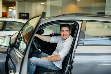 A young man is sitting in the cabin of a new car and testing it. Buying a car