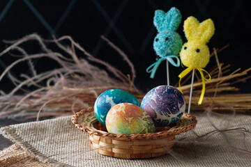 multi-colored Easter eggs of blue tones and two Easter bunny on a stick on a brown cloth background