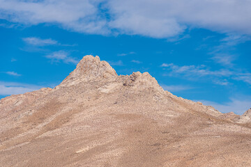 Brown desolate desert mountain peak reaching for the blue sky above.