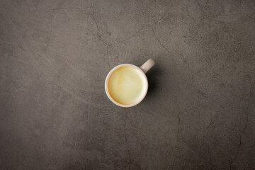 Top view of a cup of hot espresso black coffee with brown espresso coffee foam cream on the top in a white grey pastel ceramic coffee mug put on a grunge look dark color cement table background.