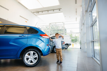 At a car dealership, a happy boy stands near a new car before buying it. Car purchase