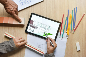Fototapeta na wymiar tablet showing architectural drawing design detail with digital pens on wood table, the concept of new technology for working of tablet with digital pen