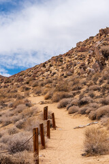 Naklejka na ściany i meble Sandy desert hiking trail in mountains under blue sky with clouds.