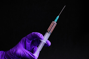 Hand with a latex glove on a black background, holding a syringe with a covid 19 vaccine.