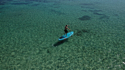 Aerial drone photo of fit man practising Stand Up Paddle or SUP in tropical exotic lake with shallow emerald water