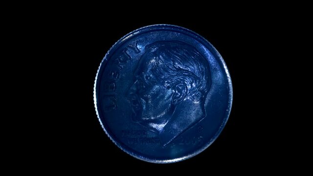On a black background, one dime coin is glitters in the rays of light. Macro. Closeup