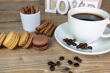 coffee break with cup of espresso and colorful macarons of chocolate, hazelnut, vanilla, salted butter. on the table cinnamon sticks