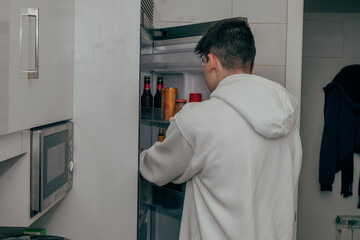 Naklejka na ściany i meble young teenager in the kitchen opening the fridge