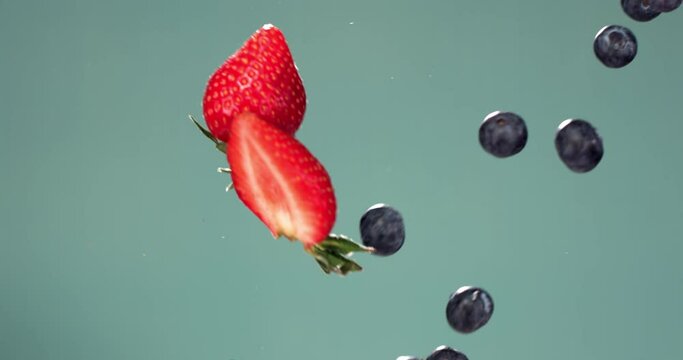SUPER SLOW MOTION fresh sliced strawberries bumping into blueberries in mid air against blue background. Shot with high speed camera, 420 FPS