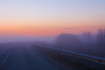 A bright dawn in pastel colors and with heavy fog greets us on a country road.