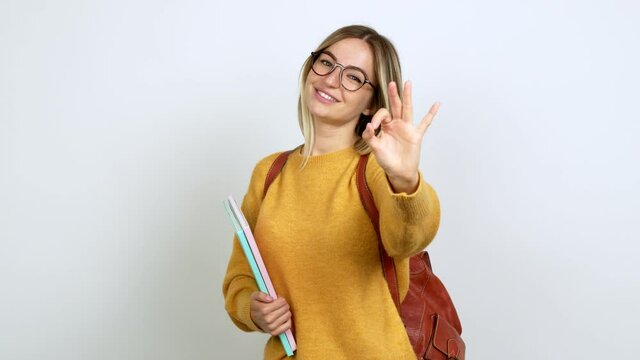 Young woman with backpack showing ok sign with fingers over isolated background