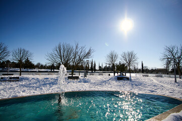 Horizontal close-up of water fountain in park surrounded by snow with blue sky and sunshine
