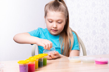A blonde child is playing with a slime. A little girl opens a jar of slime. Play a slime toy