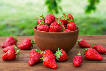Fresh juicy organic strawberries in a clay bowl. Ripe red strawberries in a bowl on a wooden table
