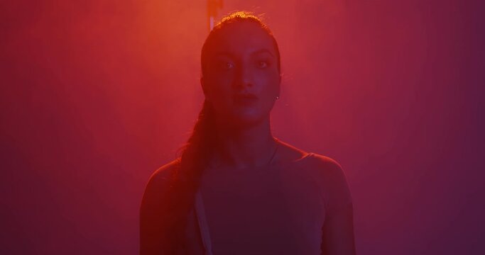 Silhouette of young mixed race girl with pigtail looking at camera in red light in studio with smoke 