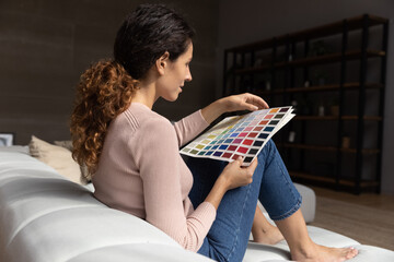 Side view of young latin woman architect designer working from home on project think on colour swatch visualize result. Female customer create flat renovation plan study palette combine colors in mind