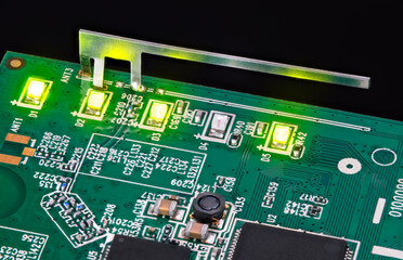 Small internal wifi antenna and shining LED lights embedded on circuit board. Light-emitting diodes, capacitors and inductor in green PCB detail with surface-mount technology of electronic components.