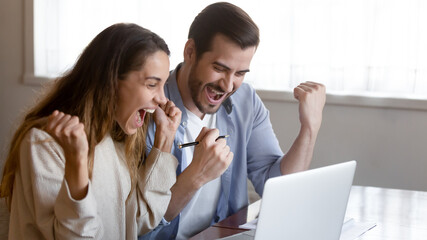 Excited millennial multiracial couple look at laptop screen triumph win online lottery on gadget....