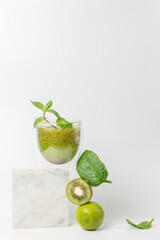 Fototapeta premium The concept of a detox cocktail of fruits and vegetables. Smoothie with kiwi, mint, lime and spinach on a stand over a white background. Vertically, copy space