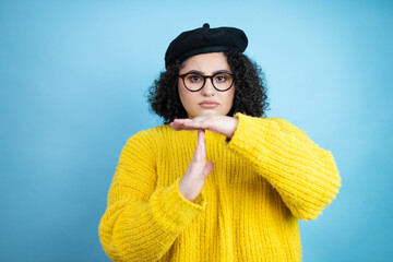 Young beautiful woman wearing french look with beret and yellow casual sweater over isolated blue...