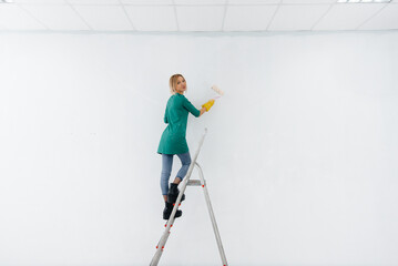 A young girl on the stairs paints a white wall with a roller. Repair of the interior.