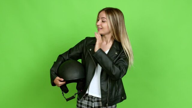 Young woman holding a motorcycle helmet standing and looking to the side over isolated background on green screen chroma key