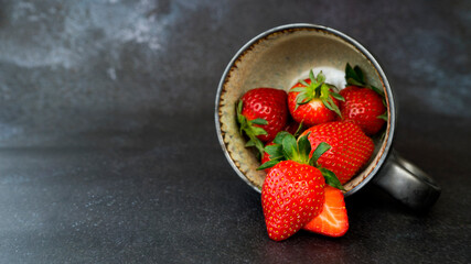 Overturned cup with fresh ripe strawberries on dark background