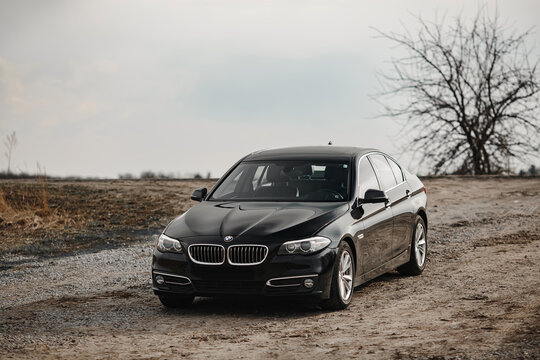 BMW 5-series F10 against the backdrop of a country road and fields. Front grill, headlights. Luxury stylish sport car banner.