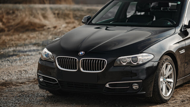 BMW 5-series F10 against the backdrop of a country road and fields. Front grill, headlights. Luxury stylish sport car banner.