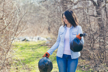 Young beautiful woman volunteer collects plastic garbage in the woods, volunteer  holding a bag of...