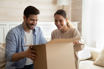 Smiling young man and woman have fun open unpack box shopping online together on internet. Happy...
