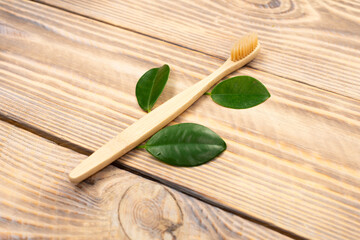 Natural eco friendly bamboo toothbrush with green tree leaves on a wooden background. Choose a wooden toothbrush. Recycling concept, no waste, no plastic, top view