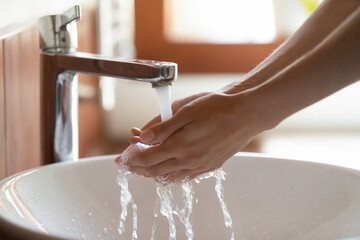 Crop close up of woman wash clean hands under tap running cold water in home bathroom. Young female...