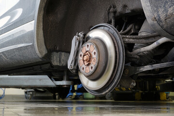 A modern car on a lift in a car service with a wheel removed. Brake disc, brake caliper. Car service and spare parts.