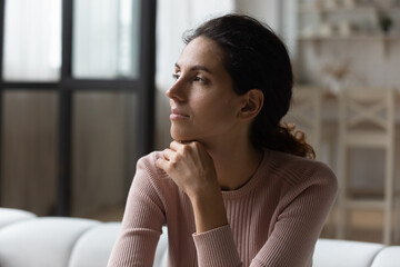 Distant memories. Calm mindful millennial hispanic female sit on sofa at studio apartment lost in...