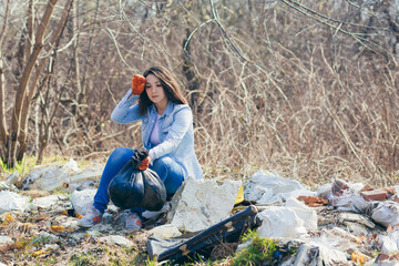 Young beautiful woman volunteer tired and resting after picking up garbage in the park, holding...