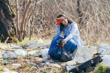 Young beautiful woman volunteer tired and resting after picking up garbage in the park, holding...