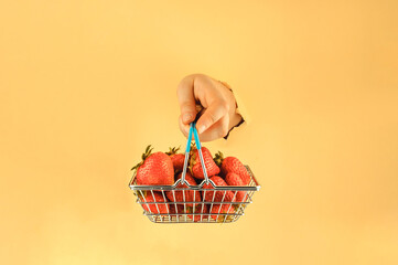 The girl holds in her hand a shopping basket with red ripe strawberries. Woman's hand in torn...