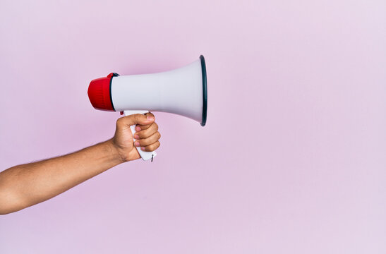 Hand of hispanic man holding megaphone over isolated pink background.