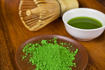 Green matcha tea in a cup with powdered matcha tea in a plate and bamboo matcha tea whisk also know as chasen on a wooden background. 