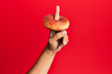 Finger of hispanic man holding donut over isolated red background.