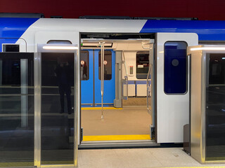 A blue electric train carriage with an open sliding mechanical door at a train station platform