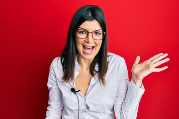 Young hispanic woman using lavalier microphone celebrating victory with happy smile and winner expression with raised hands