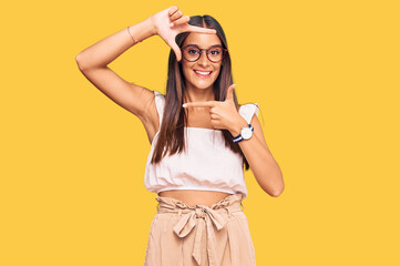 Young hispanic woman wearing casual clothes and glasses smiling making frame with hands and fingers with happy face. creativity and photography concept.