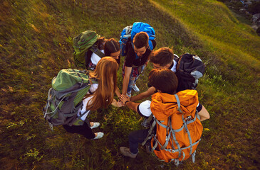 Handshake of young smiling tourists hikers standing in circle and hiking together on nature
