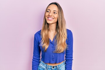 Beautiful hispanic woman wearing casual blue shirt looking away to side with smile on face, natural expression. laughing confident.