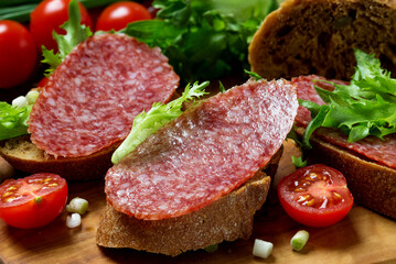 Sandwiches with dried  sausage, tomatoes, onions on a cutting board.