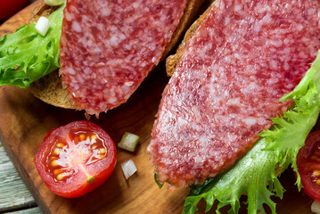 Sandwiches with dried  sausage, tomatoes, onions on a cutting board.